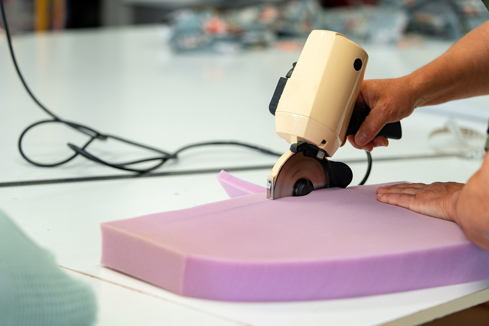 Hands of a furniture master cut a piece of foam with foam cutting machine